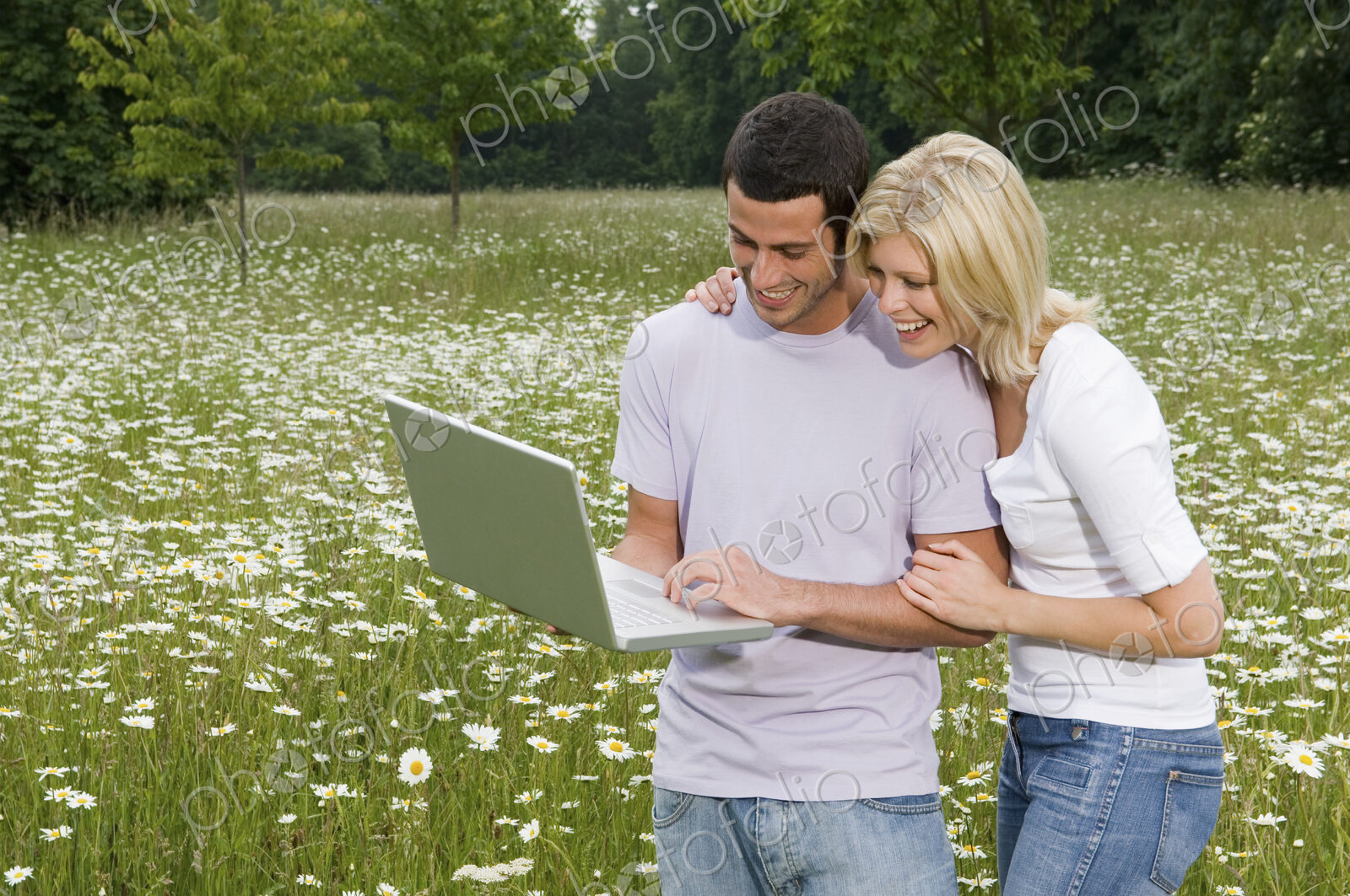 A man and woman in a flower meadow, looking at a laptop screen.