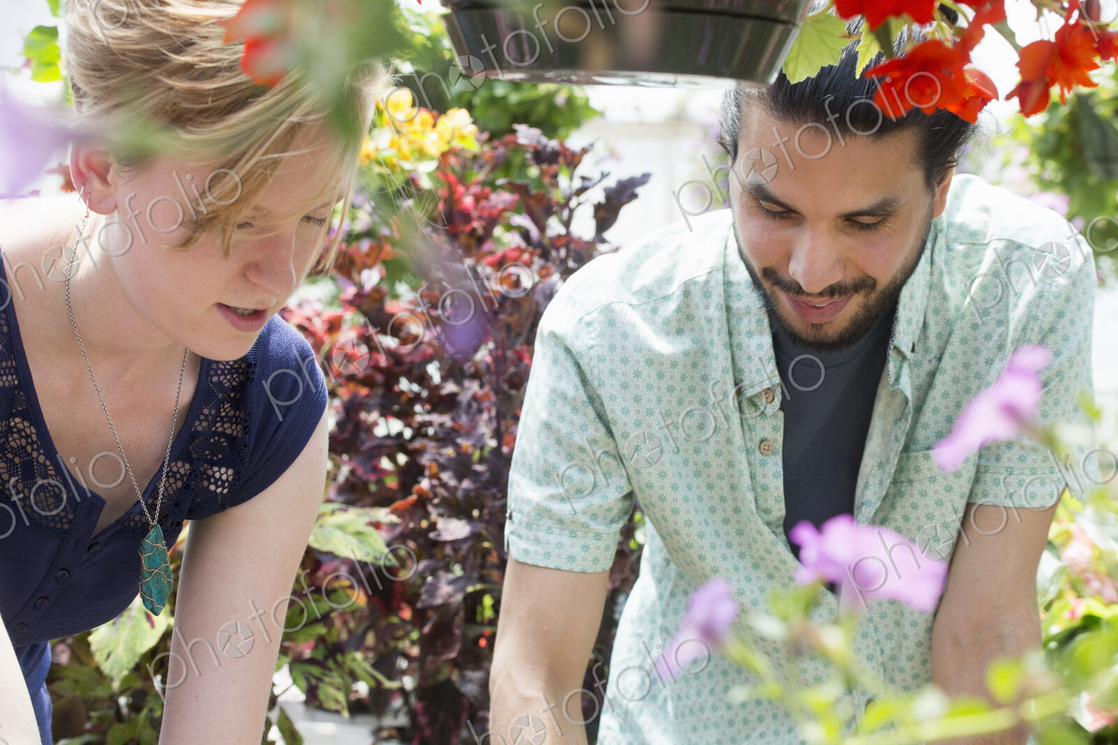 A man and woman in a garden centre, both looking down.