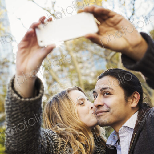 A man and woman kissing and talking a selfy outdoors in a city. A man and woman kissing and talking a selfy outdoors in a city.