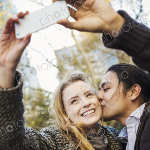 A man and woman kissing and talking a selfy outdoors in a city. A man and woman kissing and talking a selfy outdoors in a city.