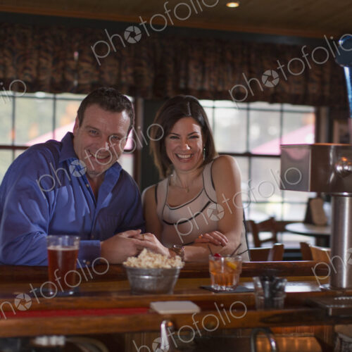 A man and woman side by side seated at a bar, smiling. On a date.