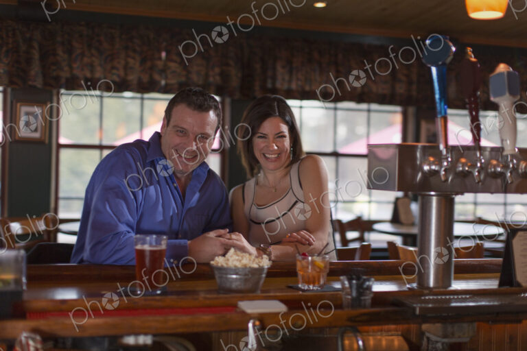 A man and woman side by side seated at a bar, smiling. On a date.