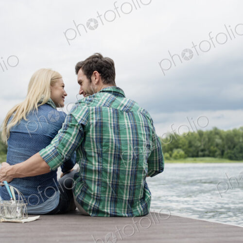 A man and woman sitting close together on a jetty by a lake. A man and woman sitting close together on a jetty by a lake.