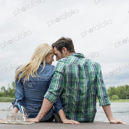A man and woman sitting close together on a jetty by a lake. A man and woman sitting close together on a jetty by a lake.
