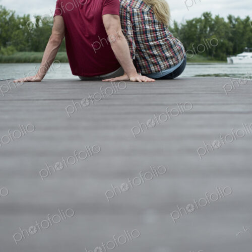 A man and woman sitting close together on a jetty by a lake. A man and woman sitting close together on a jetty by a lake.