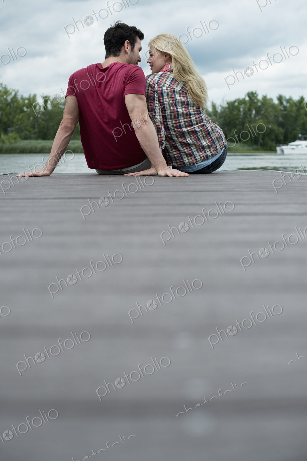 A man and woman sitting close together on a jetty by a lake.