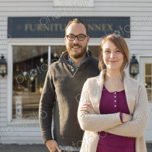 A man and woman standing outside a storefront on a street. A couple running an antique… A man and woman standing outside a storefront on a street. A couple running an antique…