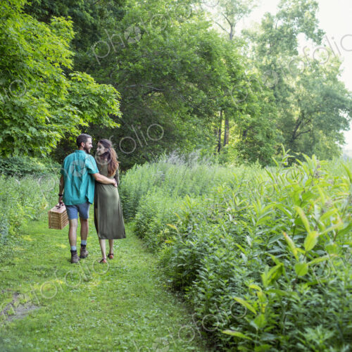 A man and woman walking through a meadow, through the long grass, carrying a picnic… A man and woman walking through a meadow, through the long grass, carrying a picnic…