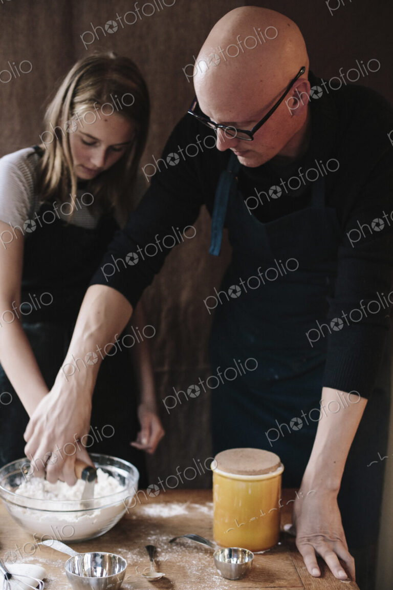A man and young girl mixing ingredients in a glass bown on a kitchen table.