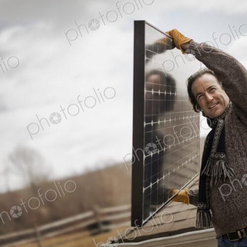 A man carrying a large solar panel across a farmyard.