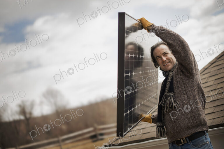 A man carrying a large solar panel across a farmyard.