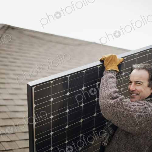 A man carrying a large solar panel across a farmyard. A man carrying a large solar panel across a farmyard.