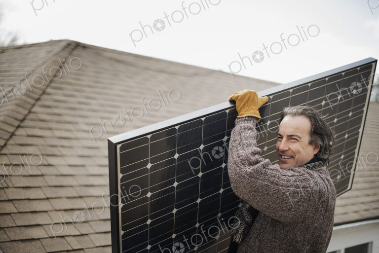 A man carrying a large solar panel across a farmyard.