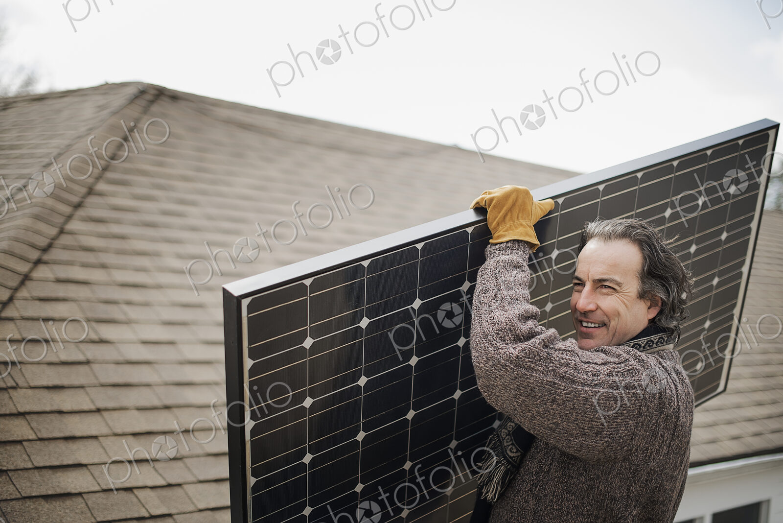 A man carrying a large solar panel across a farmyard.