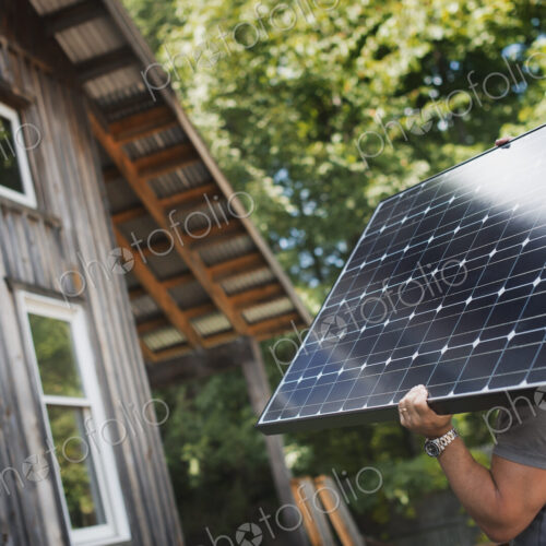 A man carrying a solar panel on a green construction site, working on a green building…