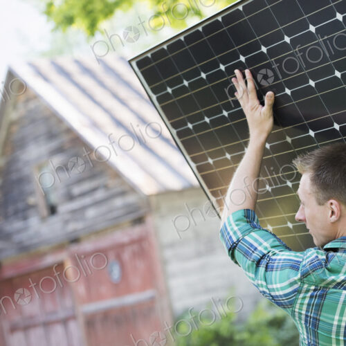 A man carrying a solar panel towards a building under construction.