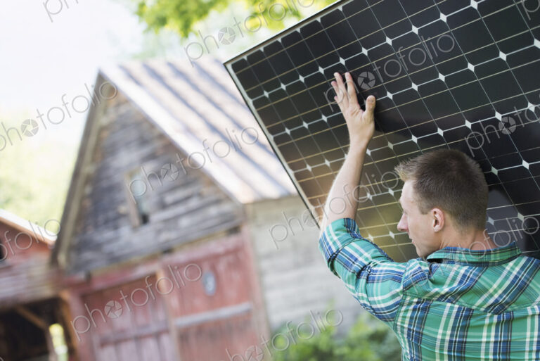 A man carrying a solar panel towards a building under construction.
