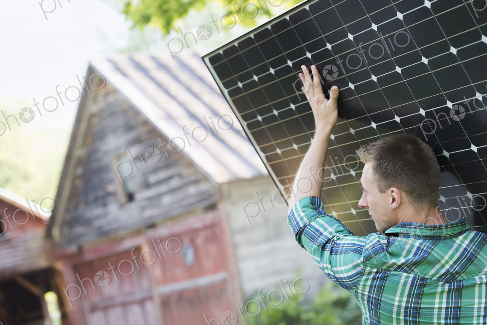 A man carrying a solar panel towards a building under construction.