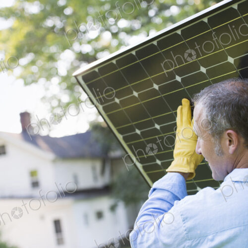 A man carrying a solar panel towards a building under construction.