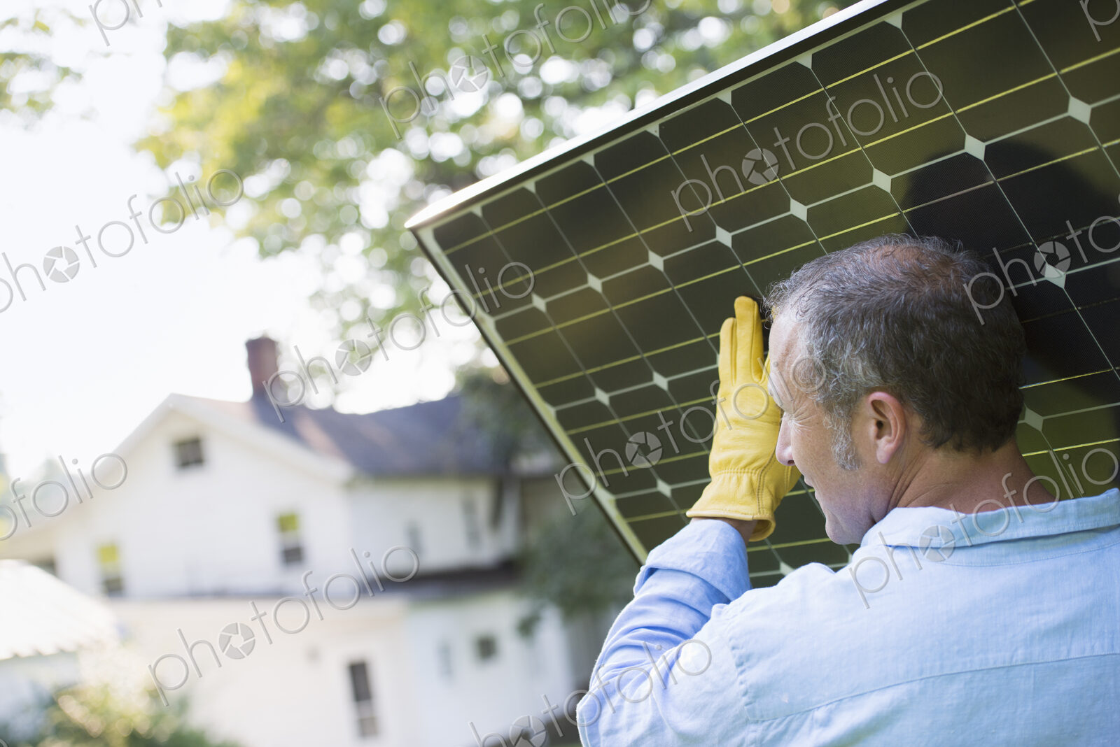 A man carrying a solar panel towards a building under construction.