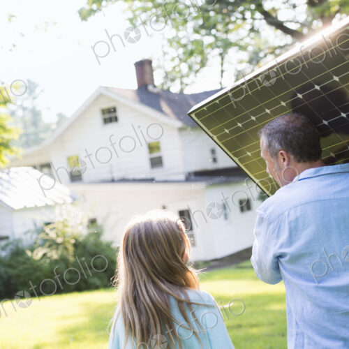A man carrying a solar panel towards a building under construction.