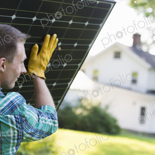 A man carrying a solar panel towards a building under construction.