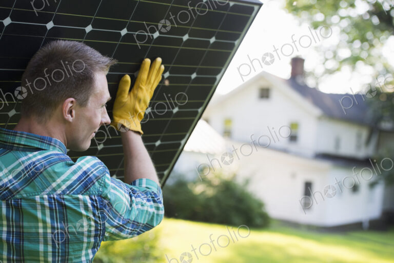A man carrying a solar panel towards a building under construction.