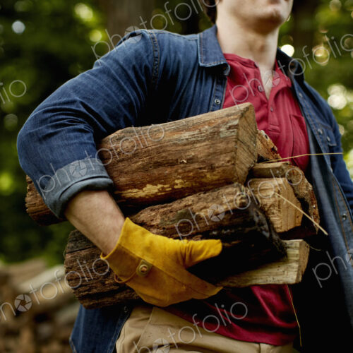 A man carrying a stack of logs under his arm.