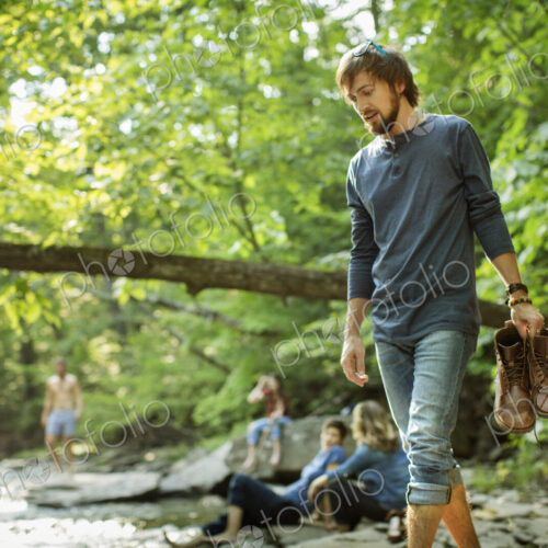 A man carrying his boots walking on the rocks by a river. A man carrying his boots walking on the rocks by a river.