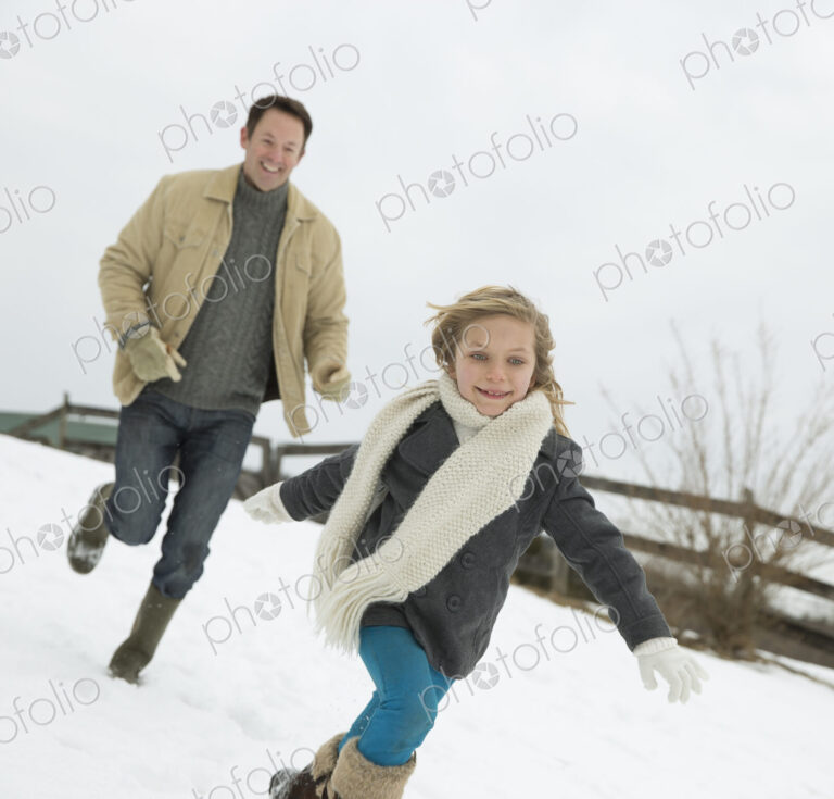 A man chasing a young girl in the snow. Farm in winter.