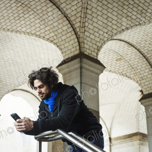 A man checking his smart phone and leaning on a stair railing. A man checking his smart phone and leaning on a stair railing.
