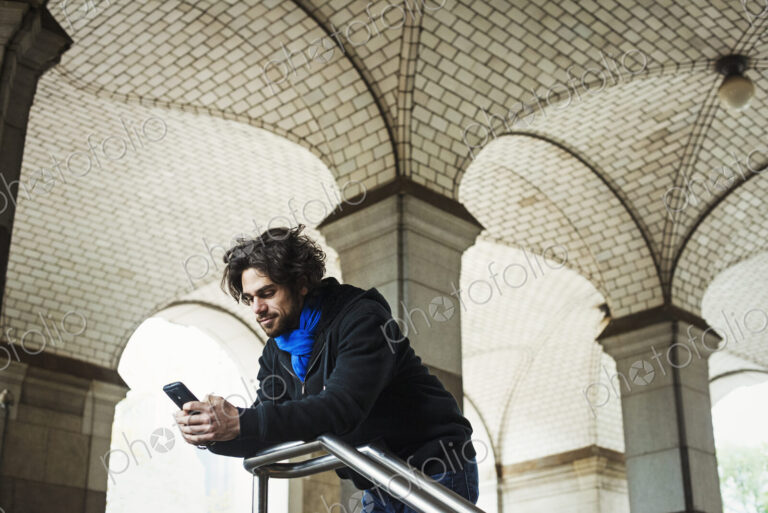 A man checking his smart phone and leaning on a stair railing.