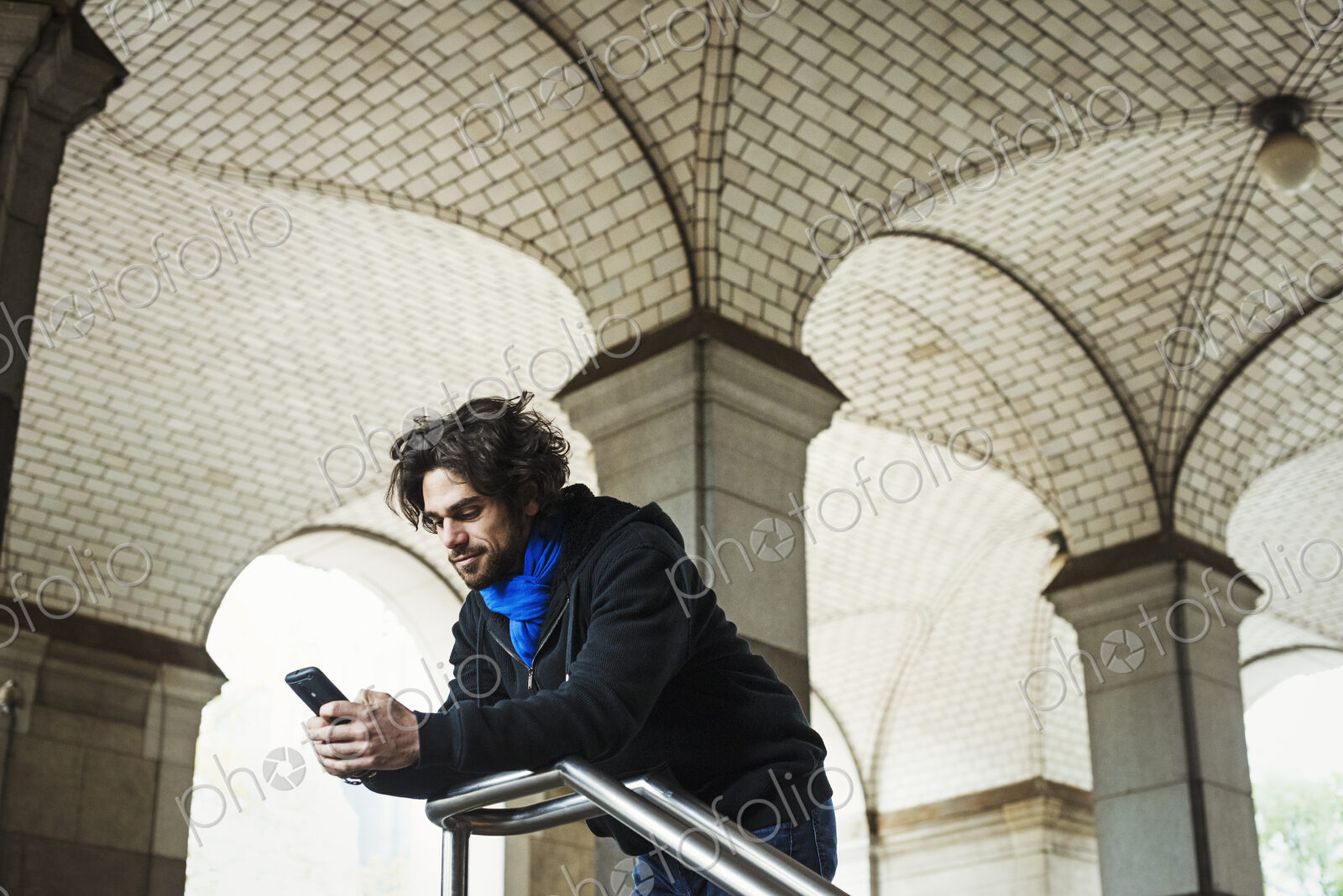 A man checking his smart phone and leaning on a stair railing.