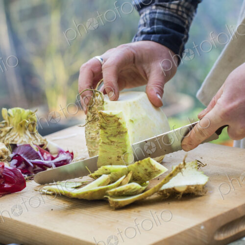 A man chopping vegetables on a board with a knife, peeling celeriac.