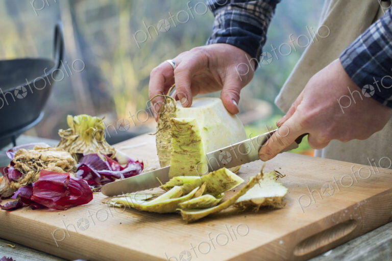 A man chopping vegetables on a board with a knife, peeling celeriac.