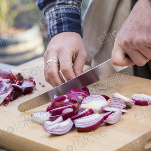 A man chopping vegetables on a board with a knife, slicing red onions.