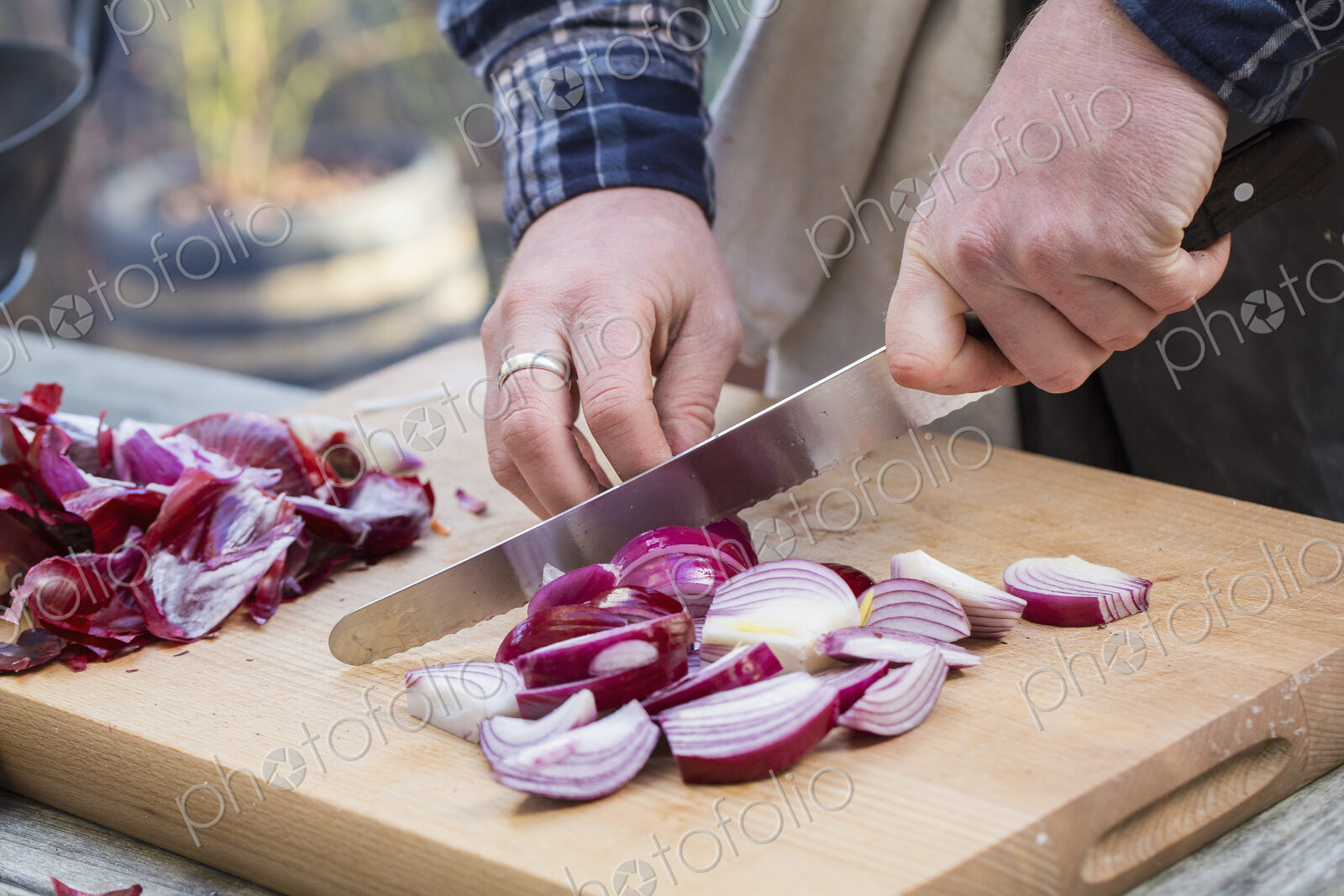 A man chopping vegetables on a board with a knife, slicing red onions.