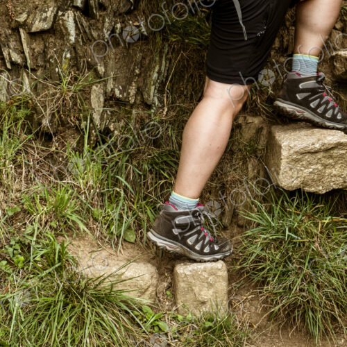 A man climbing up a set of stones set into a wall creating steps on a coastal path. A man climbing up a set of stones set into a wall creating steps on a coastal path.