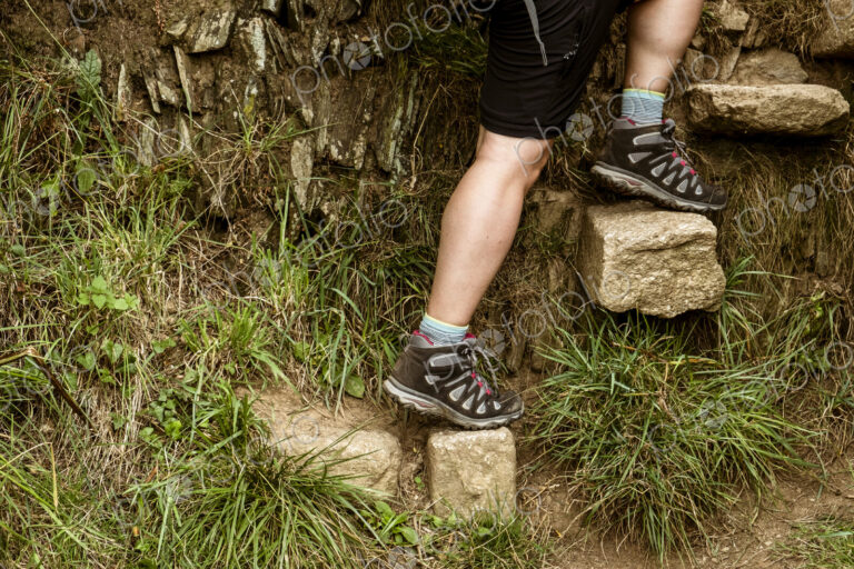A man climbing up a set of stones set into a wall creating steps on a coastal path.