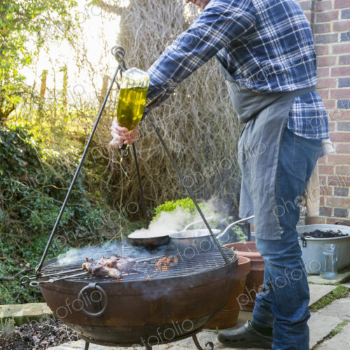 A man cooking roasting game birds over an open fire, pouring olive oil from a bottle… A man cooking roasting game birds over an open fire, pouring olive oil from a bottle…