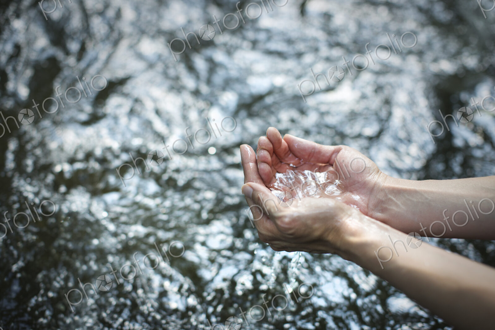 A man cupping his hands and scooping up clear water from a river.