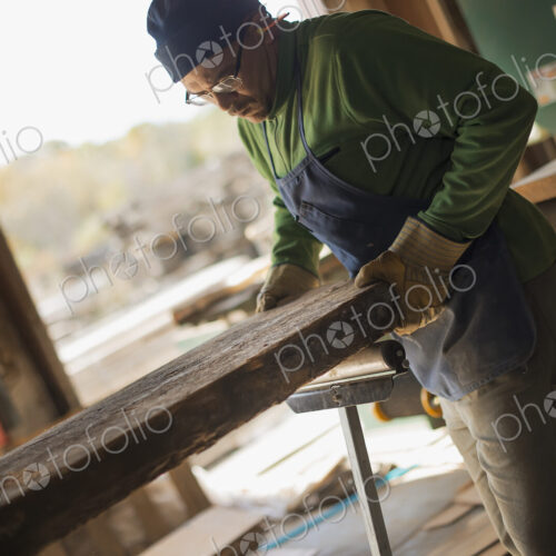 A man examining a large plank of cut wood, in a reclaimed timber yard. A workshop. A man examining a large plank of cut wood, in a reclaimed timber yard. A workshop.