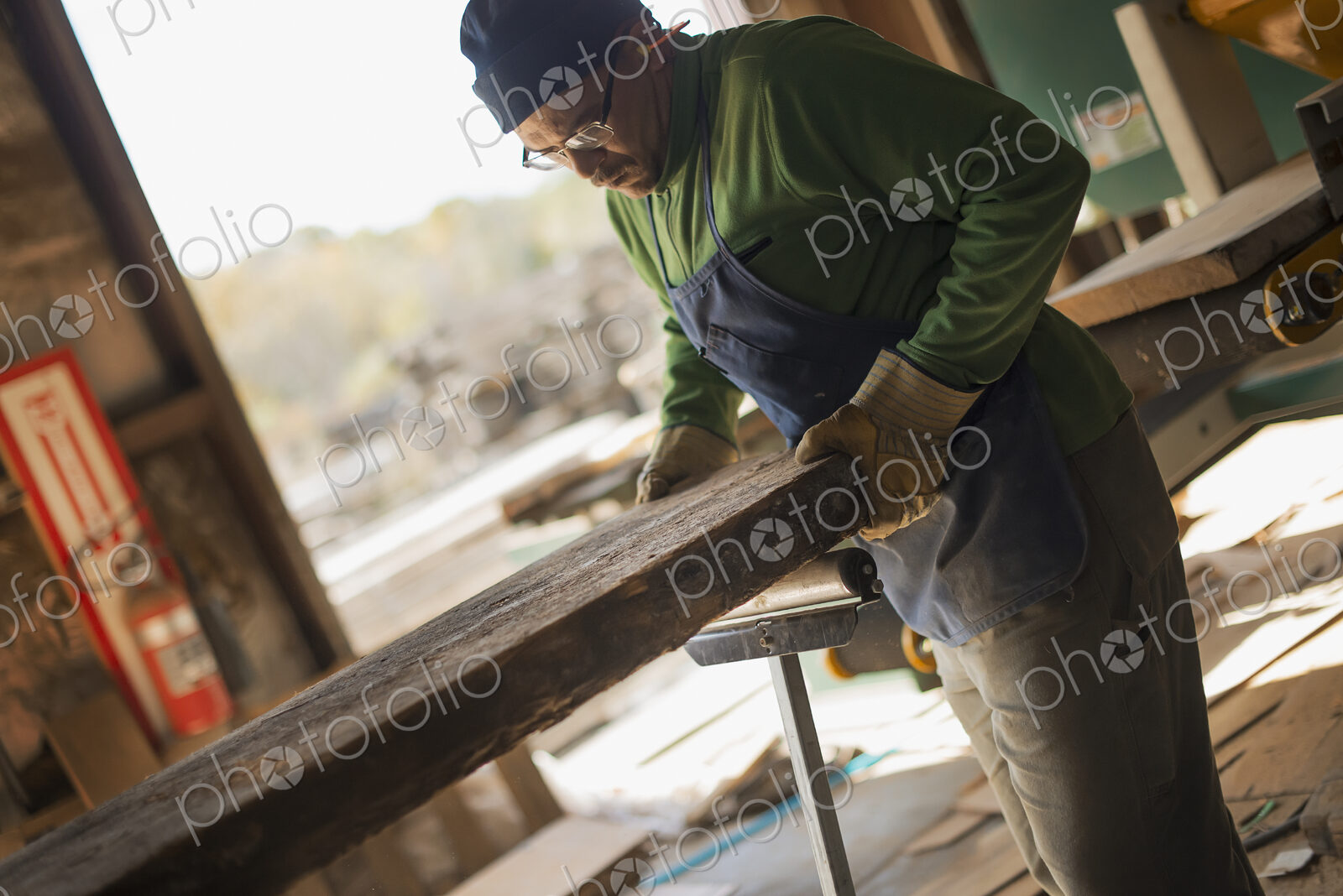 A man examining a large plank of cut wood, in a reclaimed timber yard. A workshop.