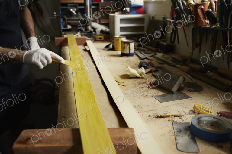 A man examining a piece of wood at a workbench.