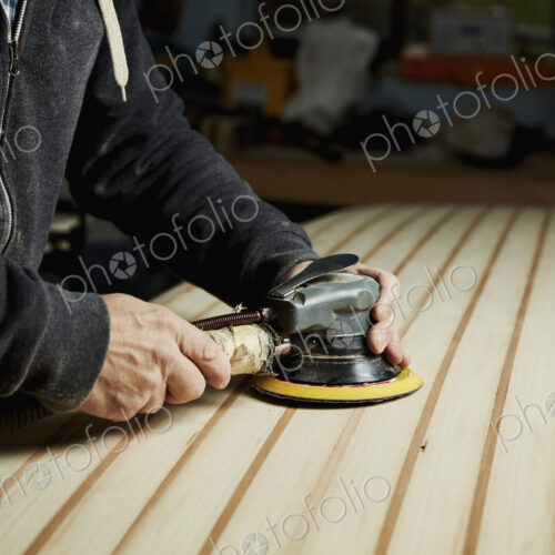 A man finishing the surface of a wooden surfboard with an electrical sander. A man finishing the surface of a wooden surfboard with an electrical sander.