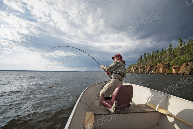 A man fishing from an open boat offshore. A fish on the line. The fishing rod bending…