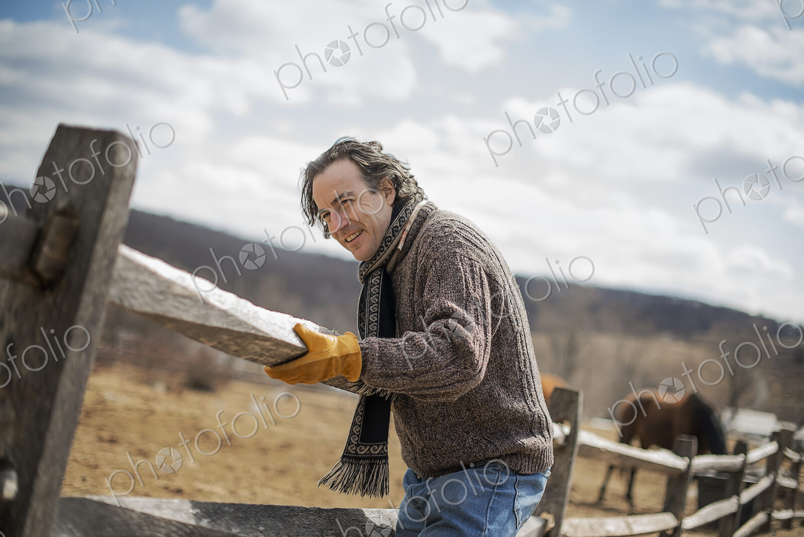 A man fixing a post and rail fence around a horse paddock.