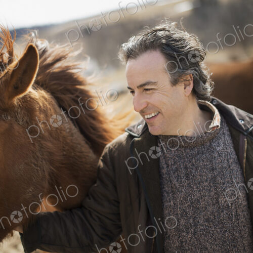A man fixing a post and rail fence around a horse paddock.