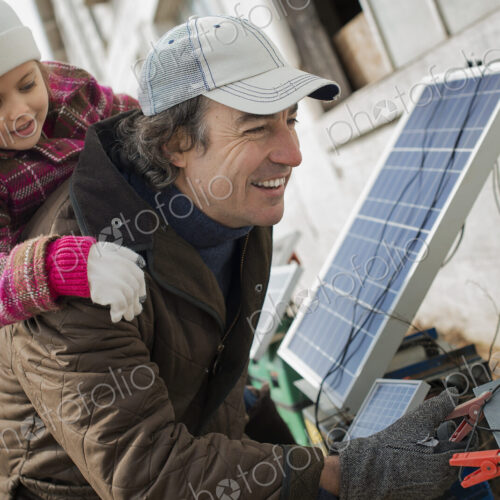 A man giving a child a piggybank while trying to connect the leads for solar power panels.
