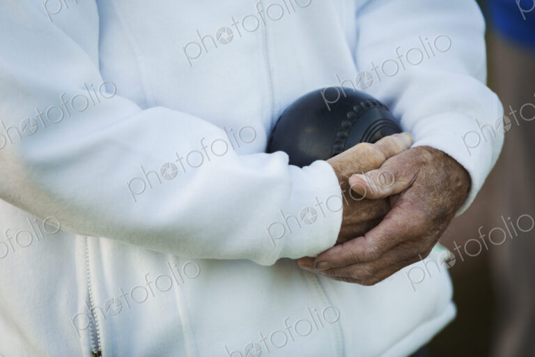 A man holding a black wooden lawn bowls ball in his hands close to his chest.